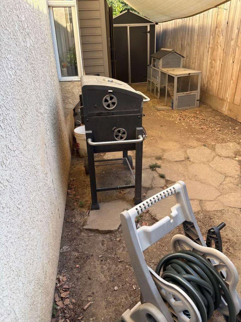 Cluttered Fresno side yard with grill and debris before junk removal